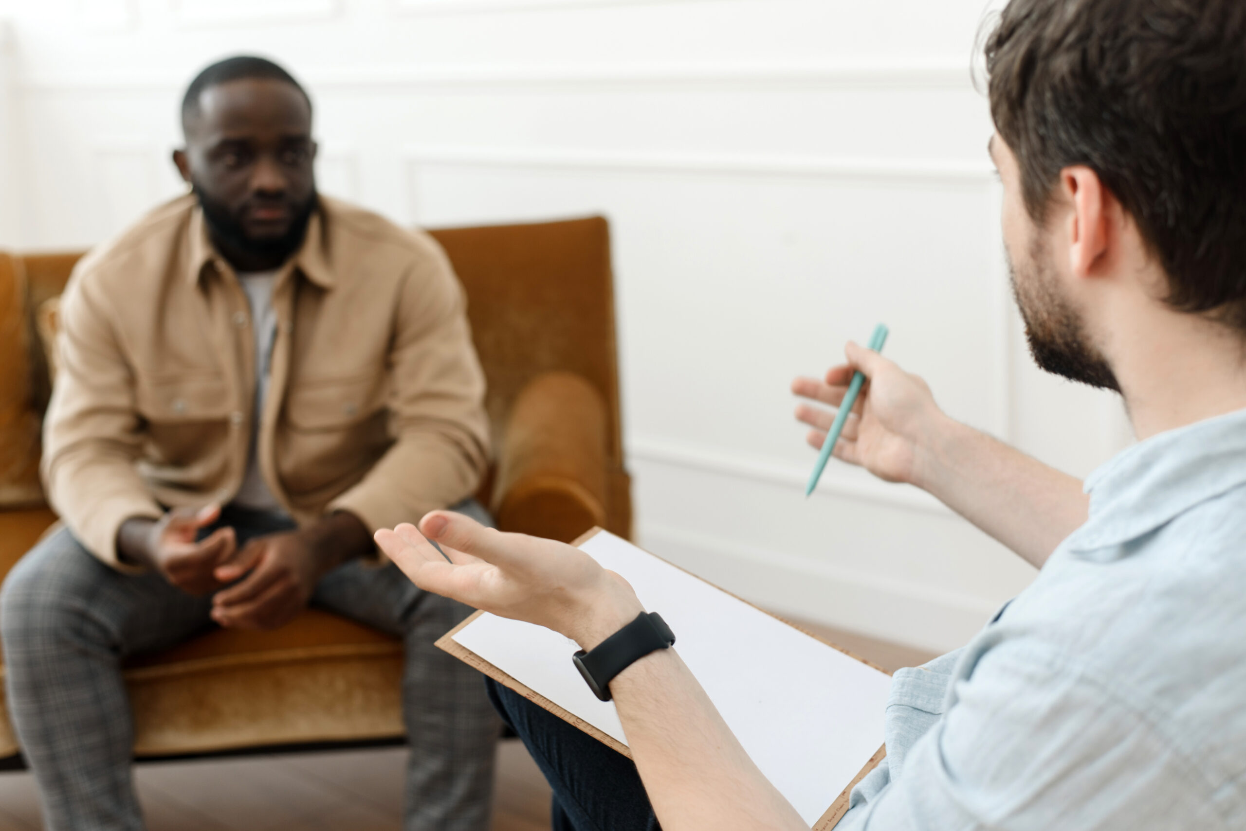 The therapist takes notes while talking to a depressed male patient and talks to an African American patient. Desperate black man suffering from nervous breakdown or depression having a session with a psychologist
