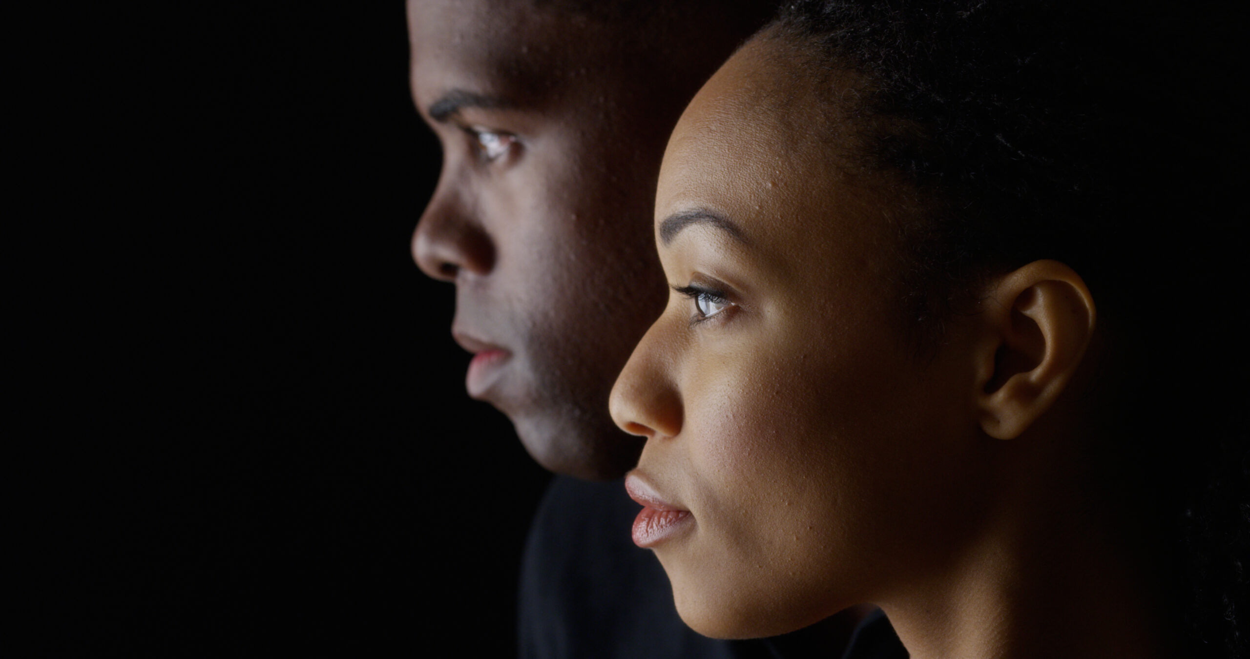Dramatic side view of two young African American people on black background