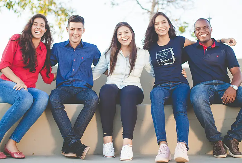 A group of college students sit on a low wall.