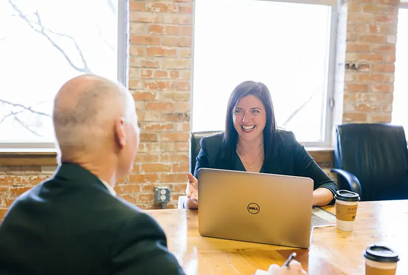 A woman smiles at a man across a desk in a meeting room