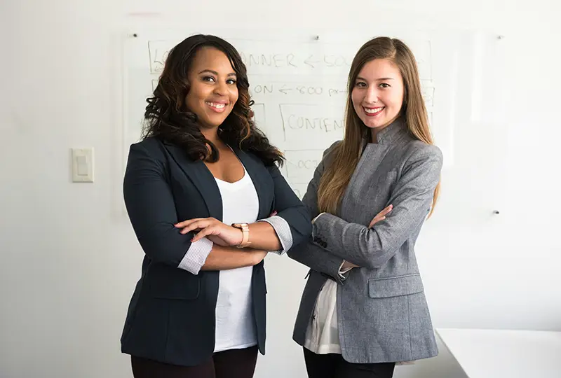 Two young professional women stand in front of a whiteboard